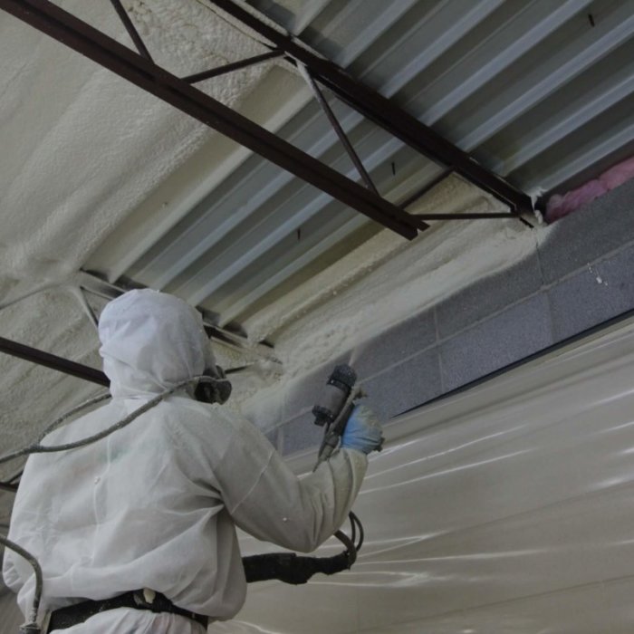 Pracownik wykonujący natrysk pianki poliuretanowej na sufit hali przemysłowej, zapewniając izolację termiczną i akustyczną.