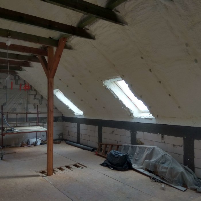Poddasze w trakcie prac remontowych z widoczną izolacją pianką poliuretanową oraz oknami dachowymi i drewnianą konstrukcją nośną.